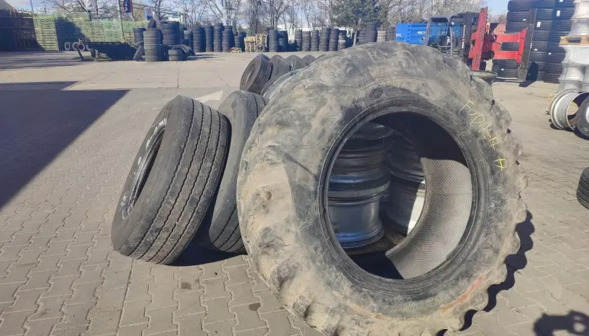 Duże opony rolnicze i samochodowe czekają na recykling opon. W tle widać stosy opon i sprzęt.