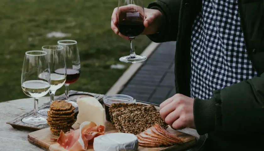 Un plateau de fromages, charcuteries et biscuits accompagne un verre de vin rouge. Une dégustation parfaite de vin et volailles en plein air.