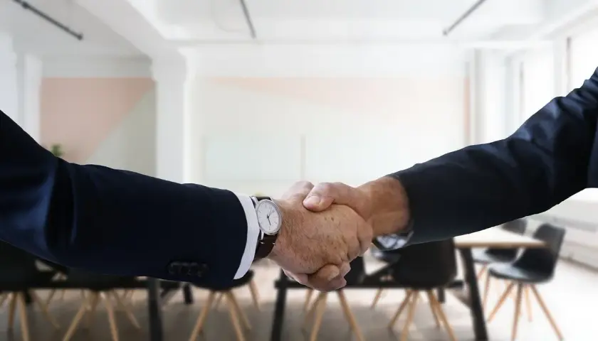 Two men in suits shake hands, a gesture of how to be professional with coworkers.