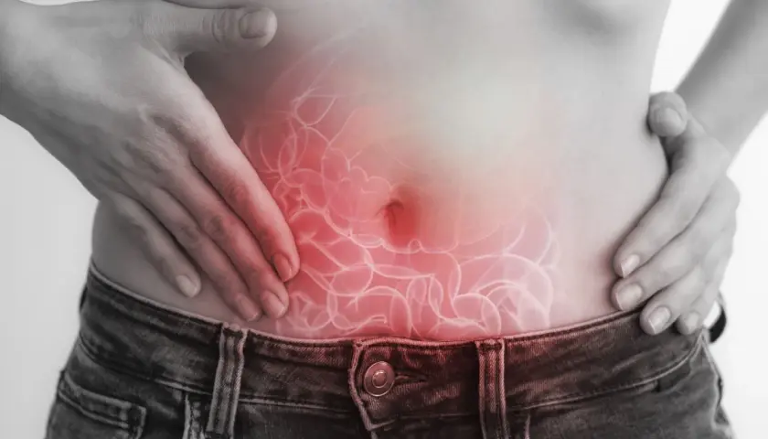 Dolore addominale, forse legato a escherichia coli in gravidanza. Mani sulla pancia con un'illustrazione degli intestini infiammati.