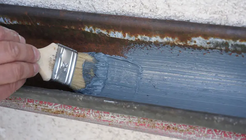 Hand streicht mit Pinsel graue Farbe auf rostige Dachrinne zum dachrinne abdichten.