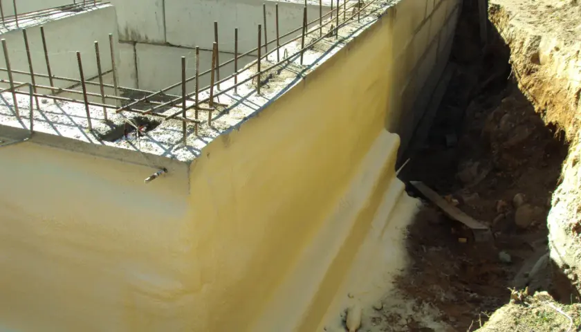 Zastosowano izolację pionową fundamentów. Widać zbrojenie i betonowe ściany fundamentowe, a obok wykop z ziemią.