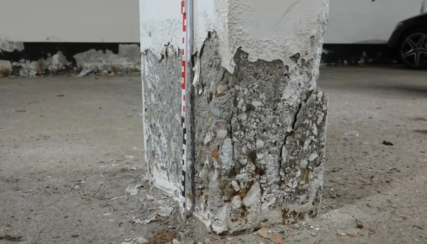Betonsäule mit starker Abplatzung und Rissen, Messlatte zur Schadensdokumentation. Die STB Decke ist hier stark beschädigt.