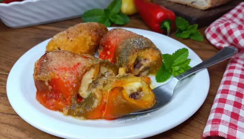 Involtini di peperoni ripieni, dorati e succulenti, serviti su un piatto bianco con menta fresca.