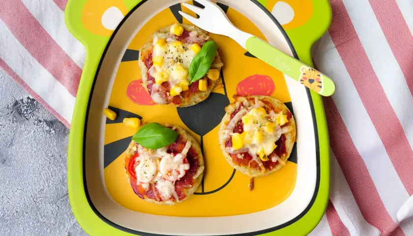 Schneller Pizzatag mit Quark: Kleine Mini-Pizzen mit Mais und Käse auf einem lustigen Teller, bereit zum Genießen.