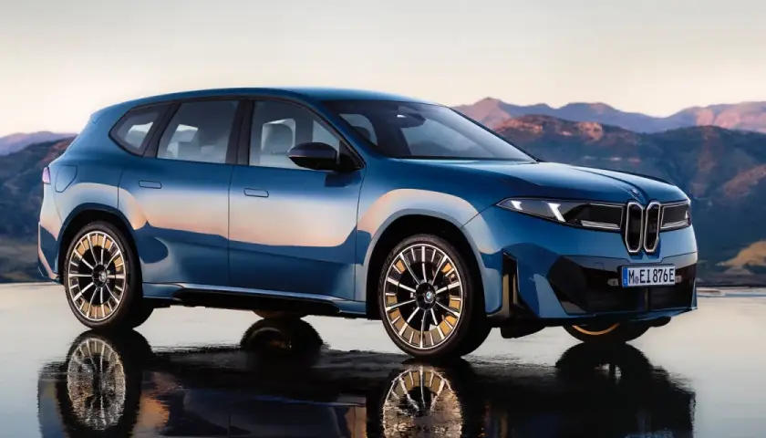 La BMW Neue Klasse blu metallizzato, con riflessi del tramonto, si staglia su uno sfondo montuoso.