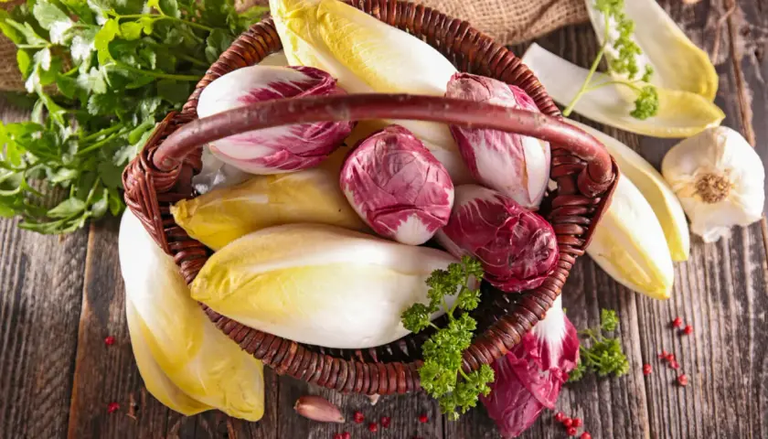 Korb mit frischem Chicorée und Radicchio, bereit, roh gegessen zu werden. Daneben liegen Knoblauch und Petersilie.