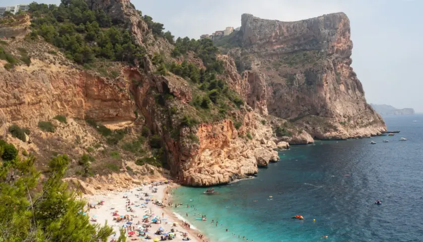 Una cala rocosa con aguas turquesas, gente disfrutando del sol y el mar. Un paraíso entre las mejores playas de la Costa Blanca.