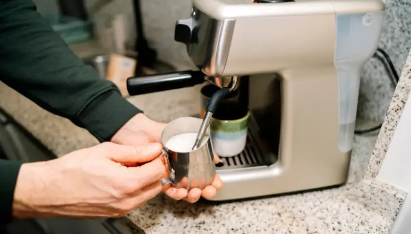 Ręce spieniają napój owsiany barista w metalowym dzbanku, przygotowując kawę.