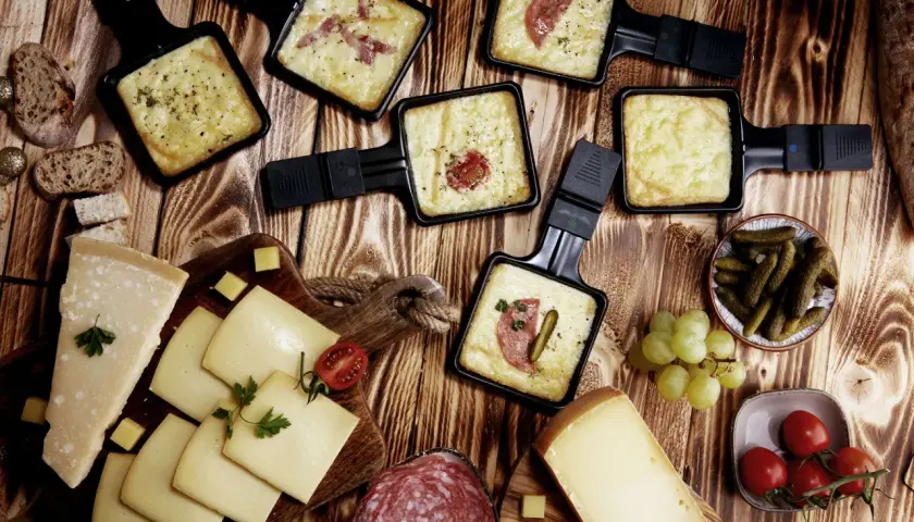 Raclette-Pfännchen mit geschmolzenem Käse, Brot, Käse, Salami, Cornichons und Trauben. Perfekt für einen gemütlichen Abend mit einem Glas Wein.
