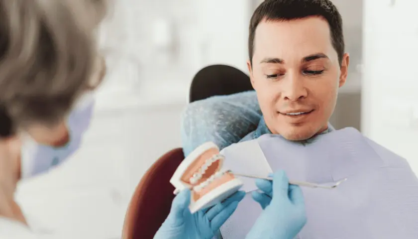 Dentysta pokazuje pacjentowi model szczęki z aparatem, omawiając, czy trzeba usuwać ósemki do aparatu ortodontycznego.