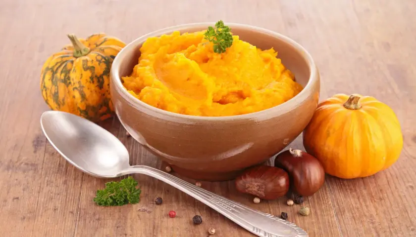 Aksamitne puree z dyni w glinianej misce, obok małe dynie, kasztany i łyżka. Idealne na jesienne dni.