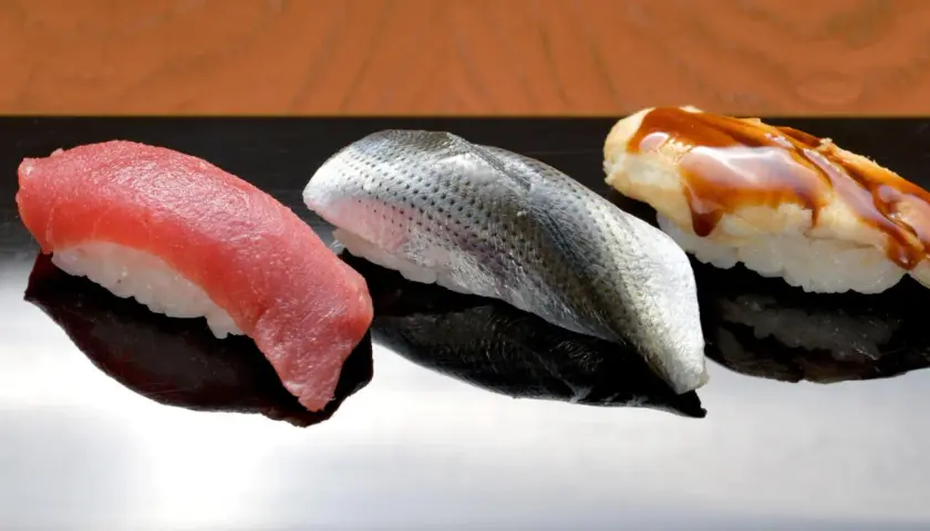 Drei exquisite Sushi-Rollen auf schwarzer Platte: roter Thunfisch, silberner Fisch mit Schuppen und ein mit Soße überzogener Fisch. Das teuerste Sushi der Welt, ein kulinarischer Genuss.