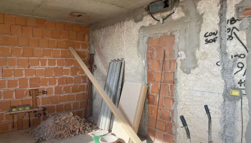 Interno di una casa in fase di ristrutturazione: pareti in mattoni a vista, cumulo di macerie, secchi, assi di legno e materiale edile.