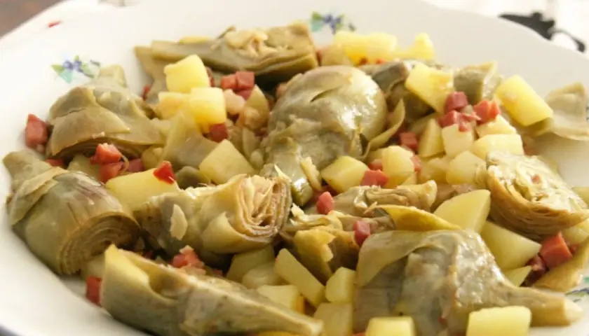 Plato de alcachofas tiernas y patatas cortadas en cubos, salpicado con trocitos de jamón. Un manjar casero.