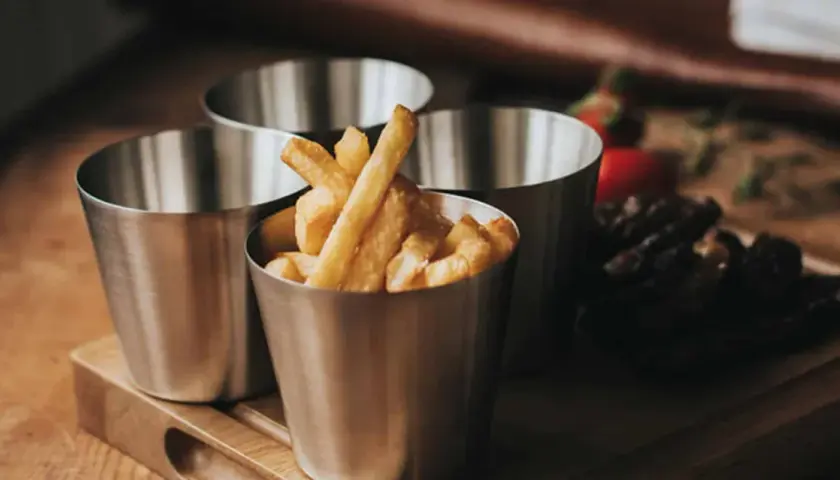 Tre metallbägare med hemmagjorda pommes frites. En bägare är fylld med gyllene pommes.