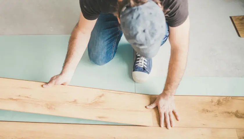 Uomo posa pannelli per come isolare il pavimento dal freddo. Sottile strato isolante azzurro sotto le assi di legno.