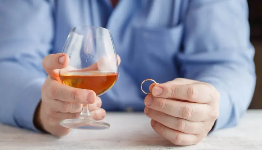 Mężczyzna trzyma kieliszek z alkoholem i obrączkę. Rozważania o rozdzielności majątkowej a alimentach na dziecko z poprzedniego związku.