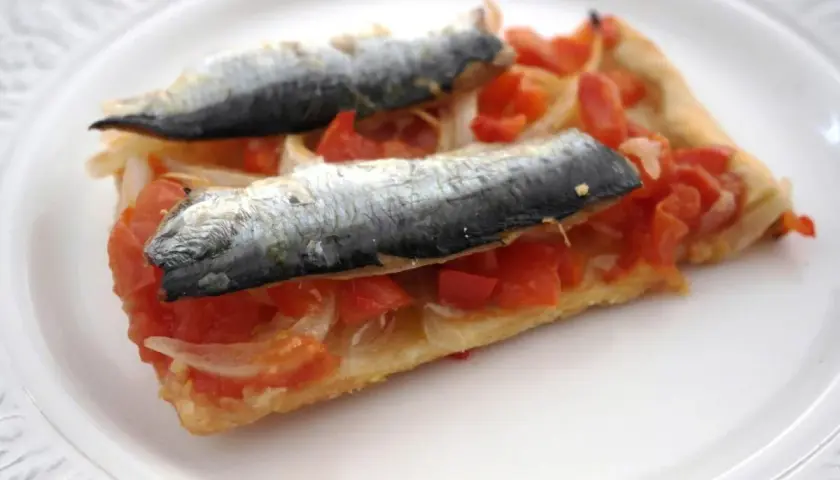 Rebanada de masa con tomate, cebolla y dos sardinas enteras, un plato que recuerda a las sardinas San Juan.