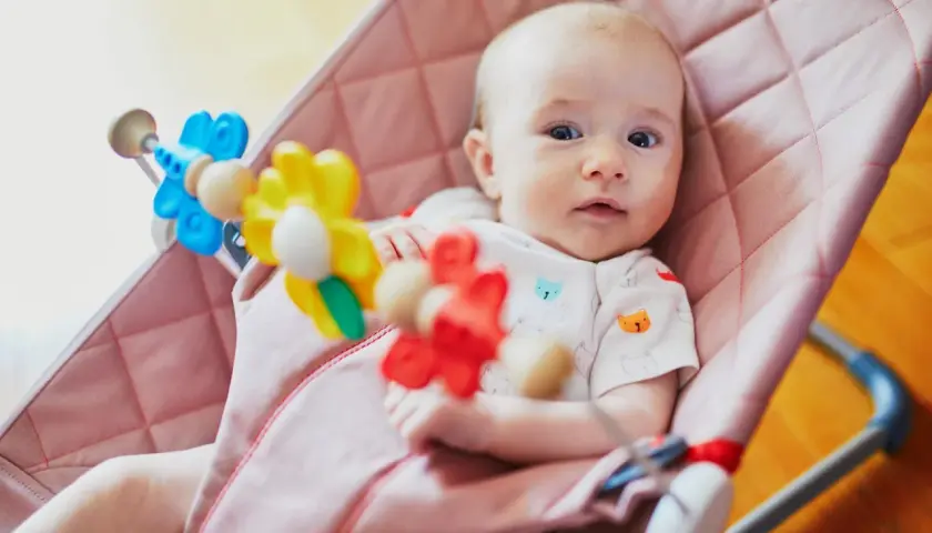 Söt bebis i en rosa babysitter vagga med färgglada leksaker.