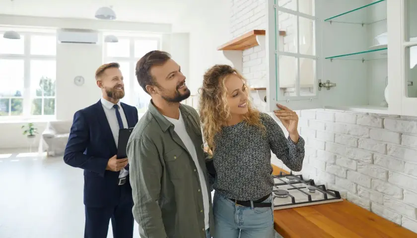 Couple inspecte une cuisine lors d'un état des lieux avant signature notaire. Un agent immobilier les accompagne.