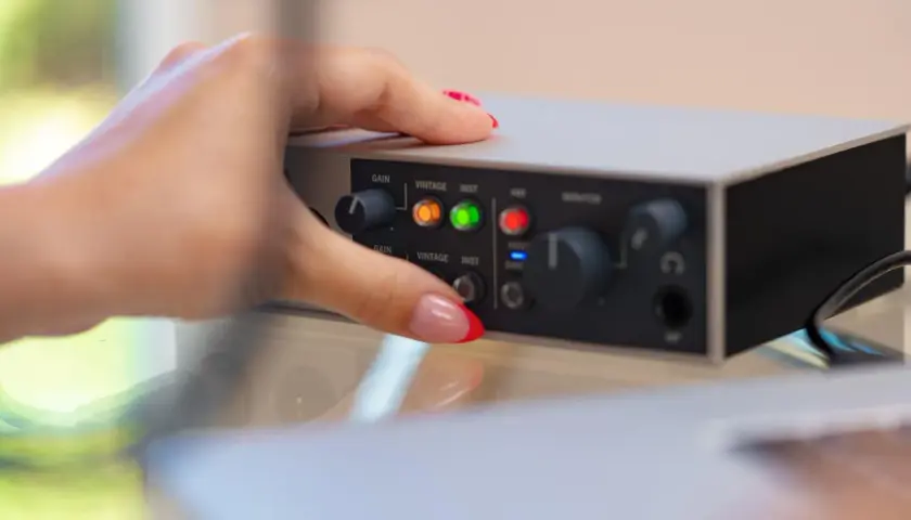 Dłoń z paznokciami ustawia pokrętło na interfejsie audio. Dowiedz się, jak podłączyć mio smartbox iii.