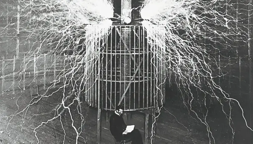 Nikola Tesla w klatce, otoczony wyładowaniami elektrycznymi, badał, kto wynalazł prąd.