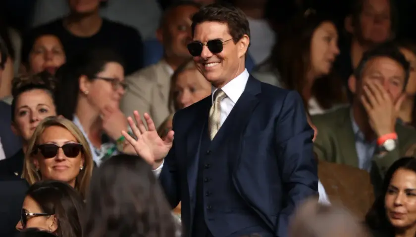 Tom Cruise w garniturze, w okularach przeciwsłonecznych, macha do publiczności. Zastanawiasz się, ile zarabia Tom Cruise?