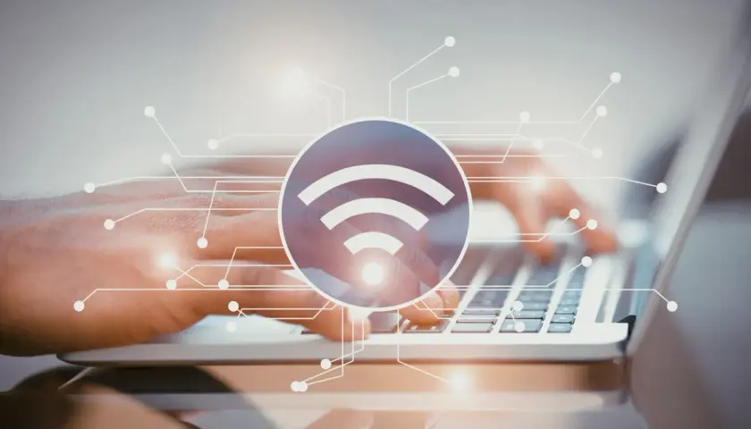 Dłonie piszące na laptopie, symbol Wi-Fi i schemat połączeń. Dowiedz się, jak sprawdzić pasmo Wi-Fi w telefonie.