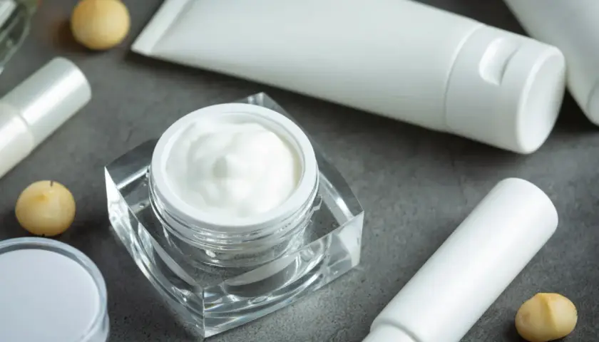 Crema blanca en un frasco de cristal, tubos y bolitas doradas. Descubre qué es el pantenol y sus beneficios para tu piel.