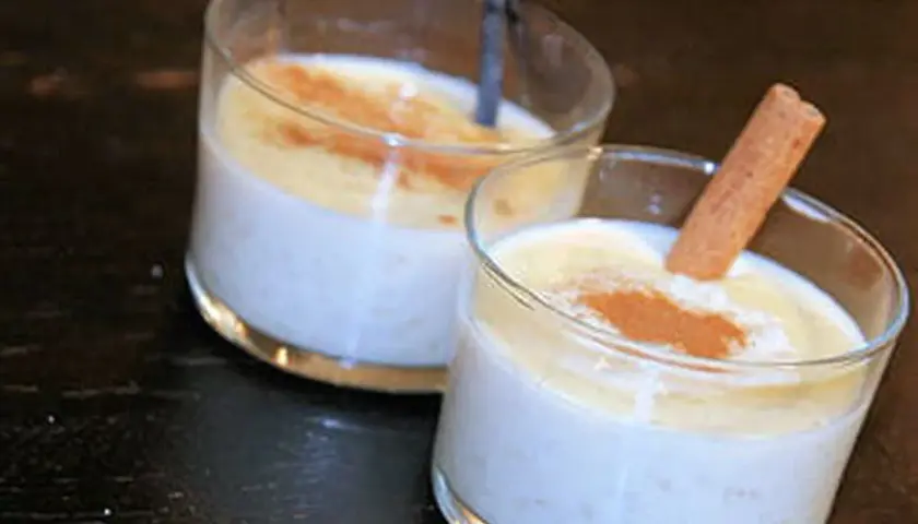 Deux verres de riz au lait crémeux, saupoudrés de cannelle. Un bâton de cannelle décore l'un des desserts, parfait pour une recette de riz au lait.