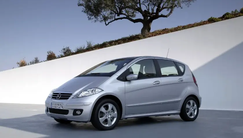 Srebrny Mercedes W169 stoi na tle białej ściany i drzewa oliwnego.