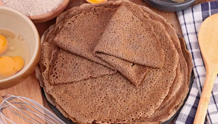 Pile de crêpes de sarrasin, avec des ingrédients pour la pâte à crêpe sarrasin : farine, œufs, beurre.