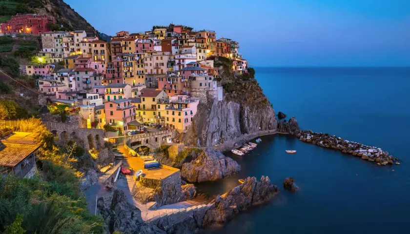 Village coloré accroché à la falaise, au crépuscule, dans le site de Cinque Terre. Bateaux dans le port, mer bleue.