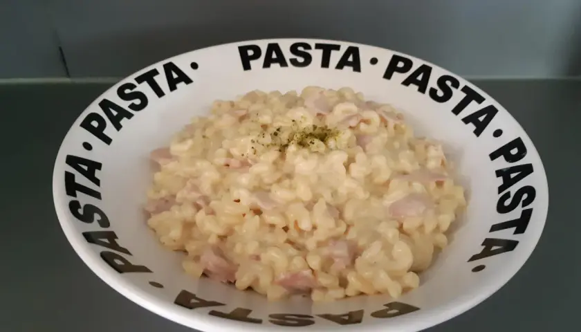 Un crémeux risotto coquillette jambon, garni d'herbes, servi dans une assiette au message "PASTA" répété.