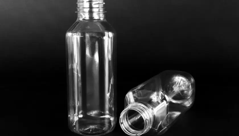 Dwie puste, przezroczyste butelki PET o pojemności 300 ml na czarnym tle. Jedna stoi pionowo, druga leży.