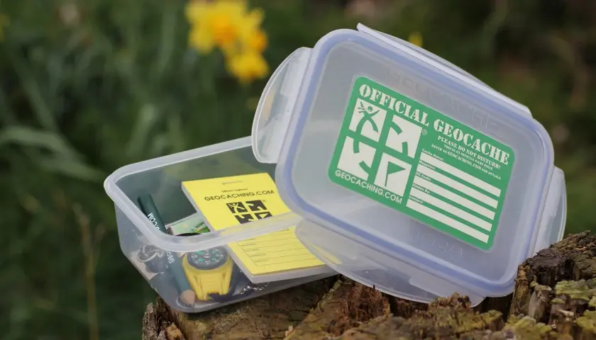 Pudełko z napisem "Official Geocache" i kompasem. To jest właśnie geocaching – zabawa w poszukiwanie skarbów.