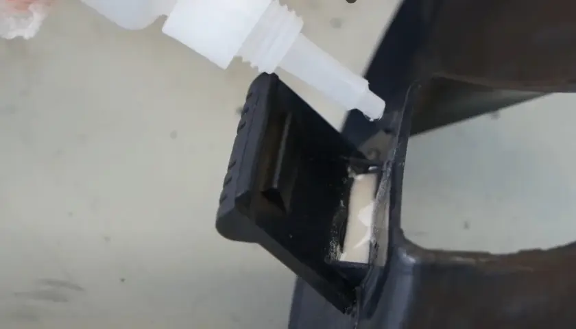 Kropla cyjanoakrylu z butelki precyzyjnie aplikowana na czarny plastikowy element, naprawiając go.