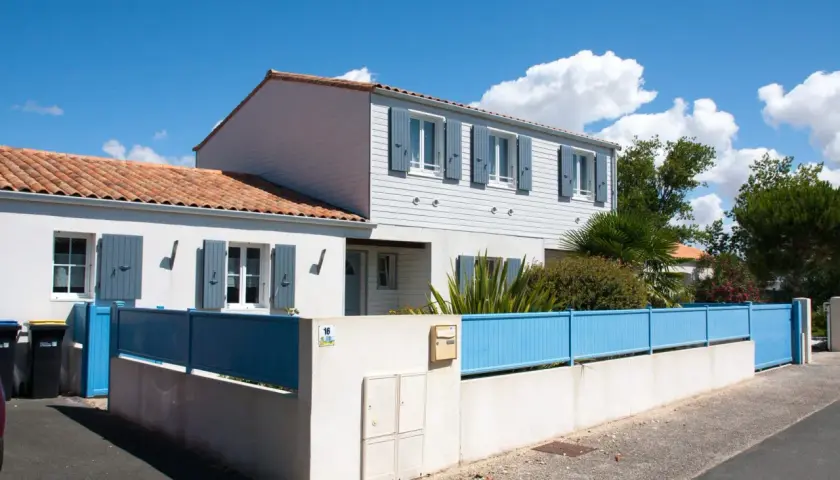 Maison année 70 rénovée, avec volets bleus et clôture assortie. Avant, elle était plus sombre.