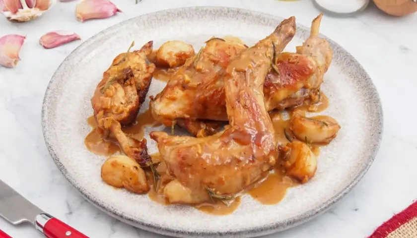 Delicioso conejo al ajillo servido en un plato, con ajos enteros y romero. Una receta tradicional lista para disfrutar.