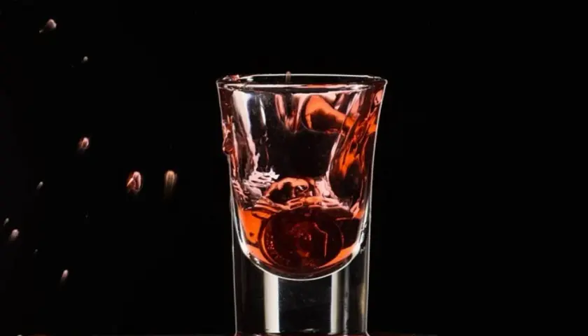 Wściekły pies drink, moneta spada do kieliszka z czerwonym płynem, tworząc fontannę.