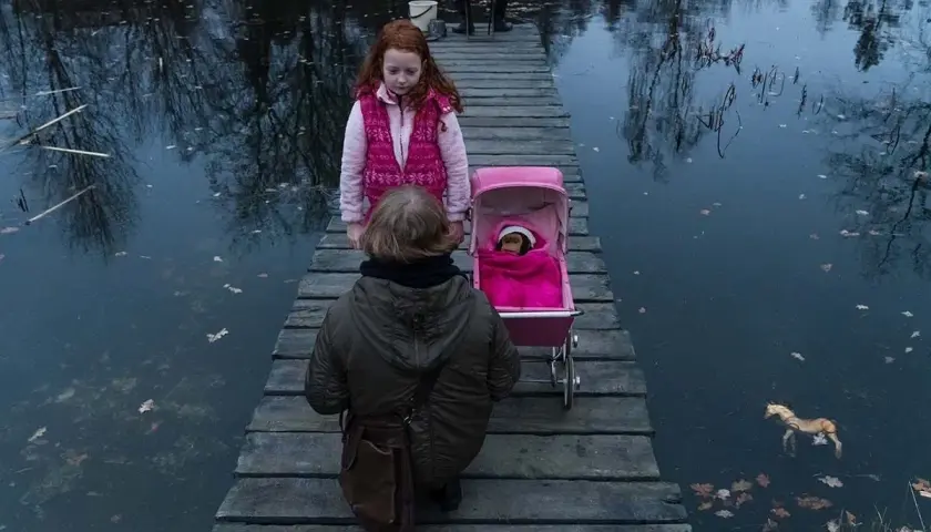 Dwie dziewczynki na drewnianym pomoście, jedna z wózkiem dla lalek, druga obok. Scena jak z filmu "ciemno prawie noc".