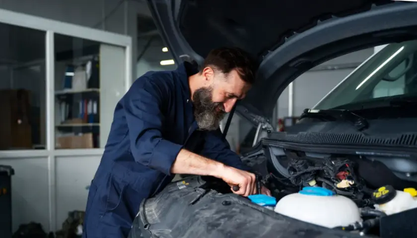 Mechanik z brodą pracuje przy silniku. Zastanawiasz się, ile kosztuje wymiana chłodnicy w samochodzie?