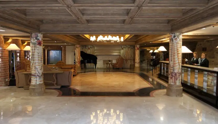 Eleganckie lobby hotelowe z fortepianem, recepcją i dwoma pracownikami.