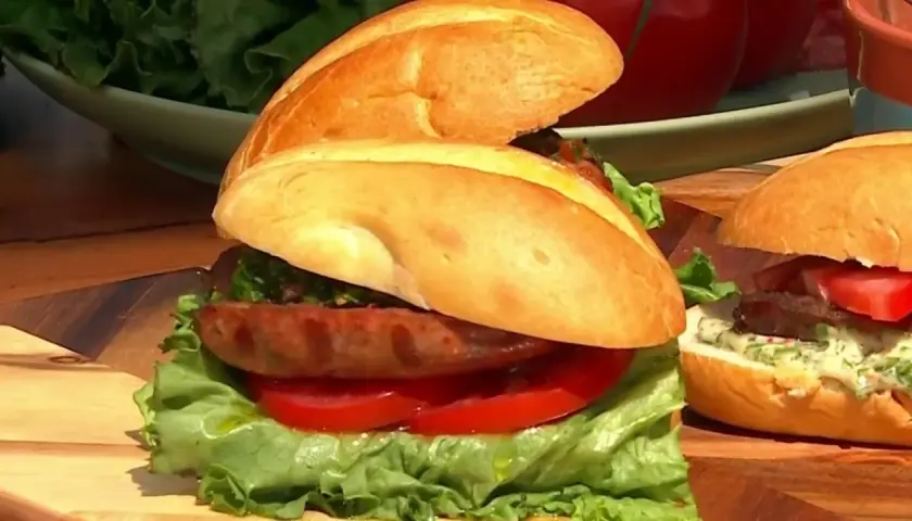 Sandwich de salchicha con lechuga, tomate y salsa chimichurri, con sus ingredientes frescos listos para servir.