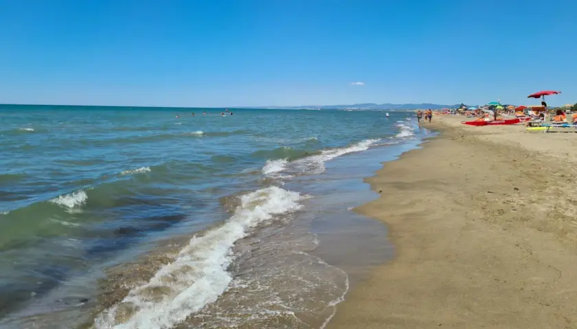 Plage de Fregene, mer bleue, sable doré, parasols et baigneurs profitant du soleil.