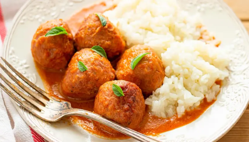 Albondigas a la jardinera con arroz blanco, decoradas con hojas verdes. Un plato casero y apetitoso.