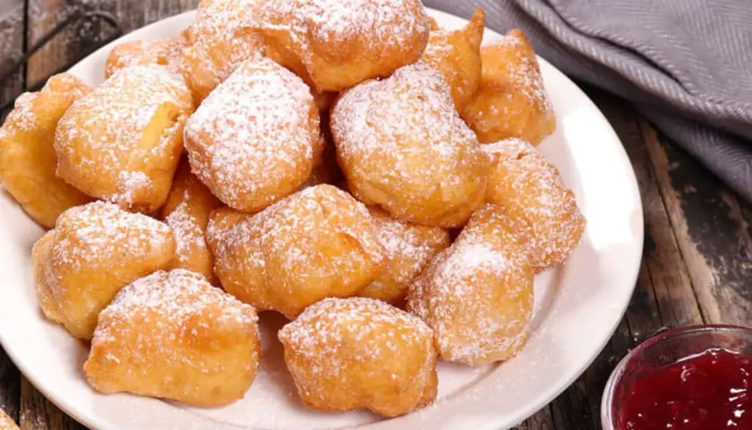 Une assiette de beignets banane saupoudrés de sucre glace, prêts à être dégustés avec une confiture de fruits rouges.