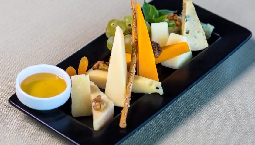 Piatto nero con vari formaggi, uva, noci, albicocche secche, grissini e una ciotolina di miele. Perfetti abbinamenti formaggi e frutta per un aperitivo.