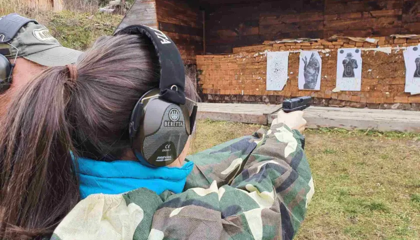 Strzelanie z broni na strzelnicy. Kobieta w słuchawkach ochronnych celuje z pistoletu do tarcz.
